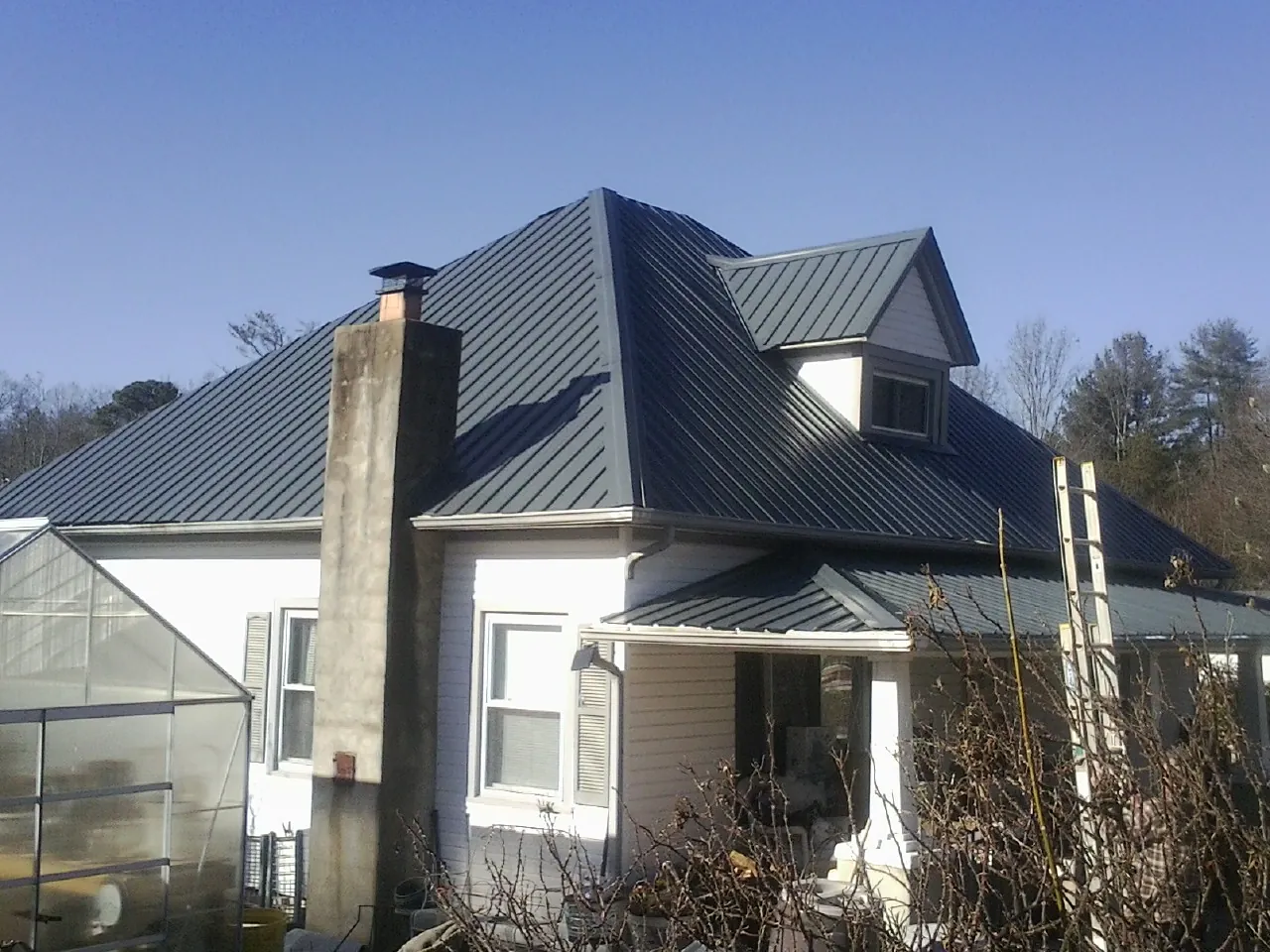Dark blue standing seam metal roof on a white farmhouse with dormer — Slate & Tile Roof Repair by Roofing Brothers in Amazonia