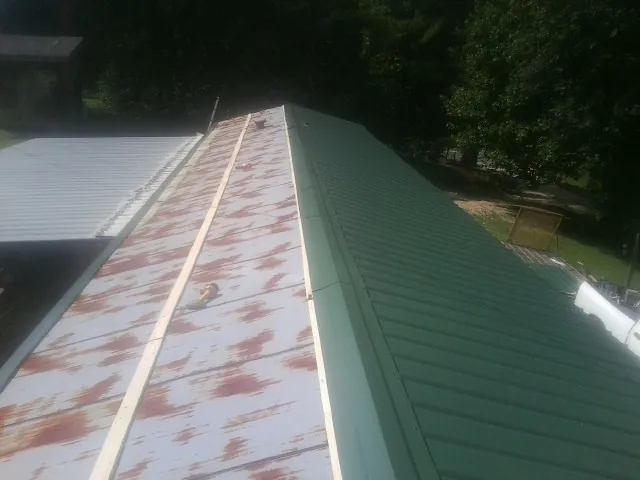 Old rusted panels beside newly installed green metal roofing — Wind Damage Roof Repair by Roofing Brothers in Amazonia