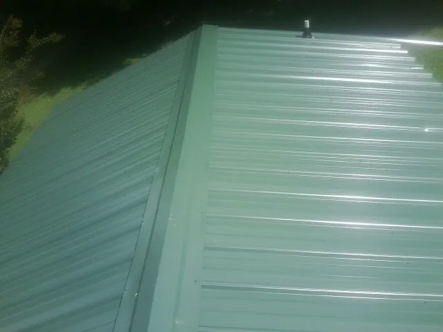 New green metal panels meeting at the ridge of a roof — Flat Roof Repair work by our crew in Amazonia