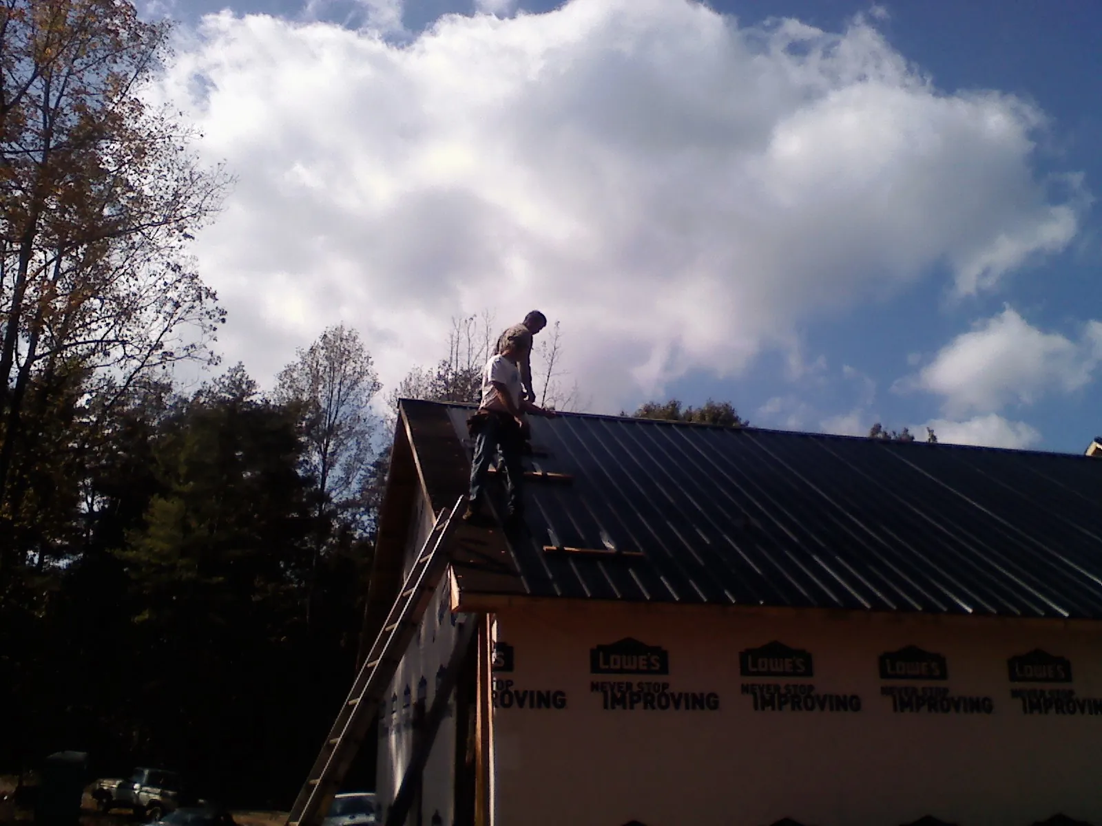 Roofer fastening dark metal panels high against a cloudy sky, from a Roof Inspection job in Amazonia