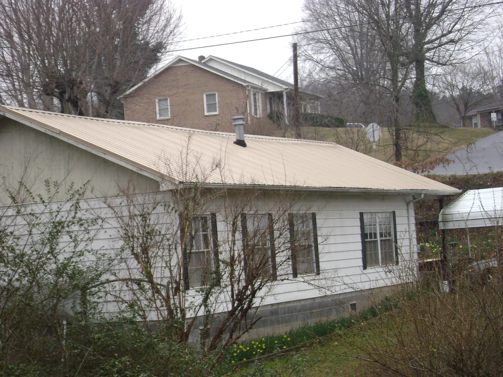 Tan metal roof on a white sided house set into a hillside — Commercial Roofing by Roofing Brothers in Amazonia